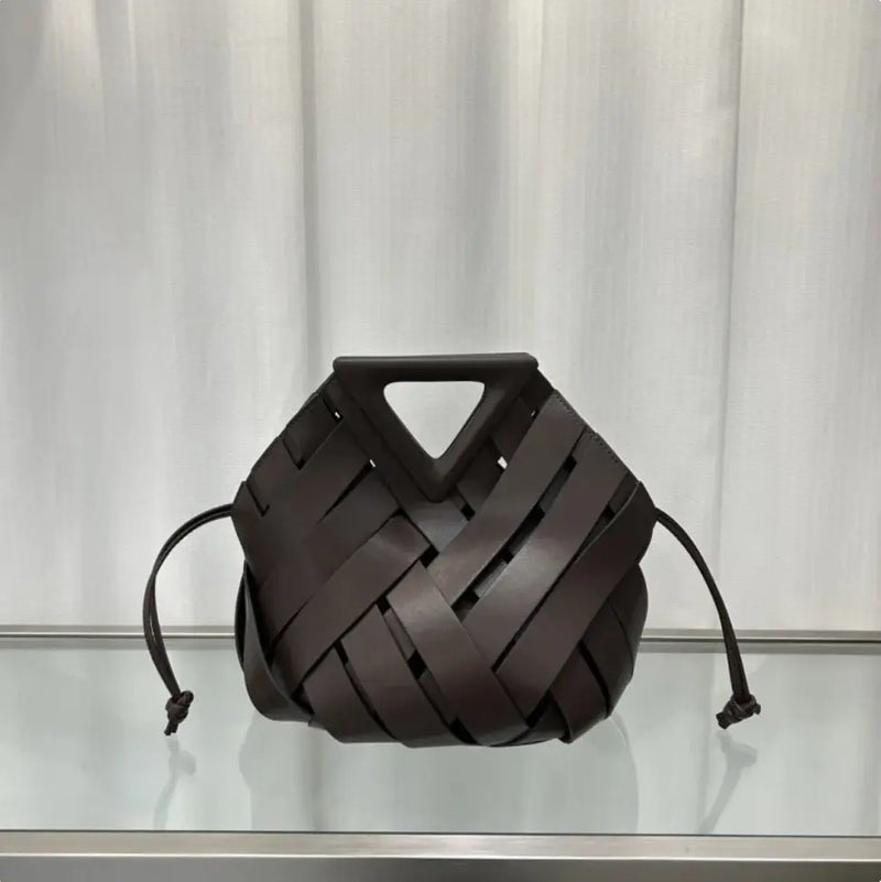 Brown woven handbag on a reflective surface with a neutral background