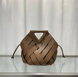Brown woven handbag on a reflective surface with a neutral background