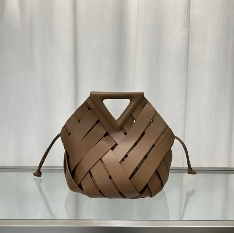Brown woven handbag on a reflective surface with a neutral background