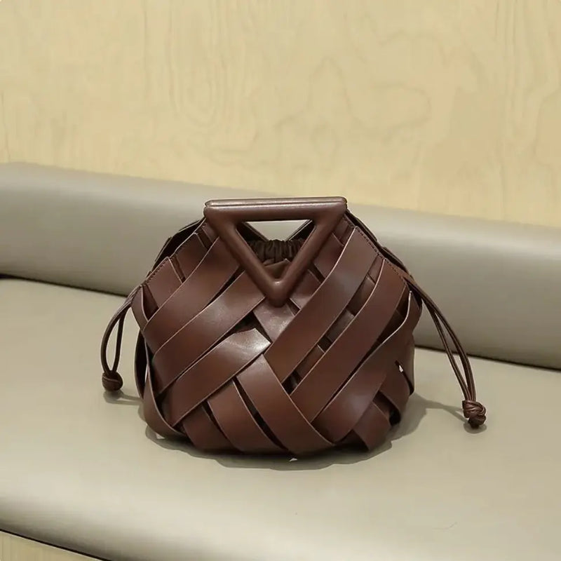 Brown woven handbag with a triangular handle on a beige surface