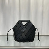 Black woven handbag on a reflective surface with a neutral background