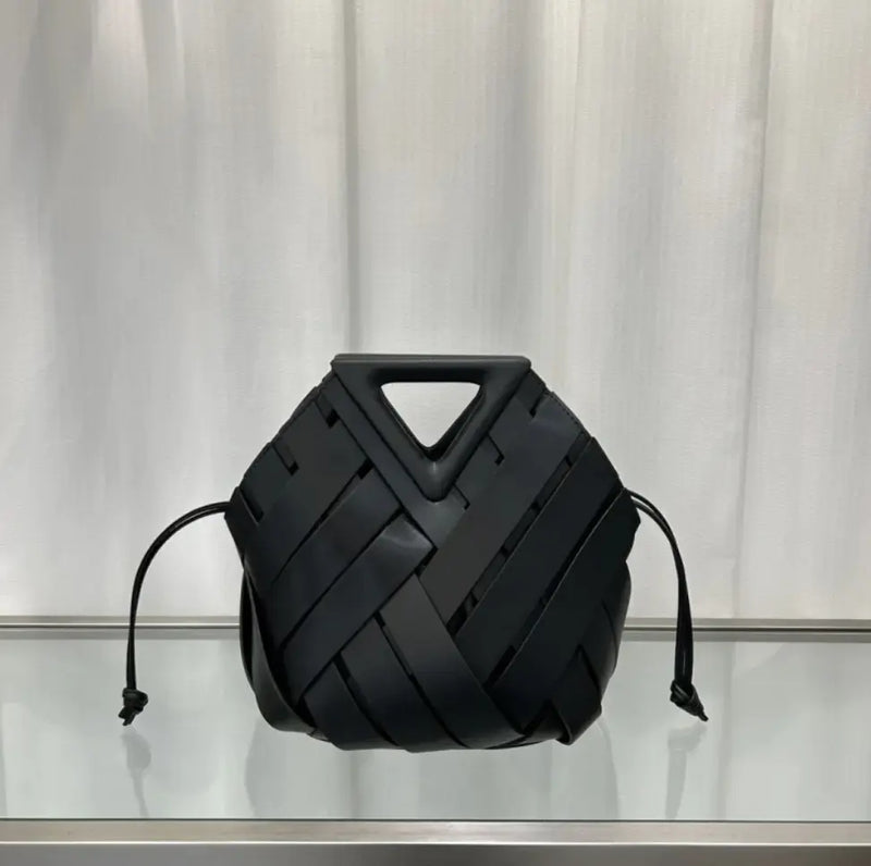 Black woven handbag on a reflective surface with a neutral background